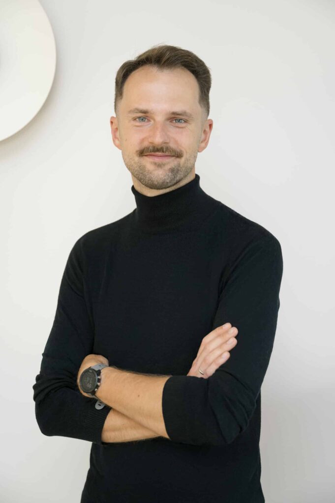 Maciej Kowalski, psycholog, stoi z założonymi rękami.