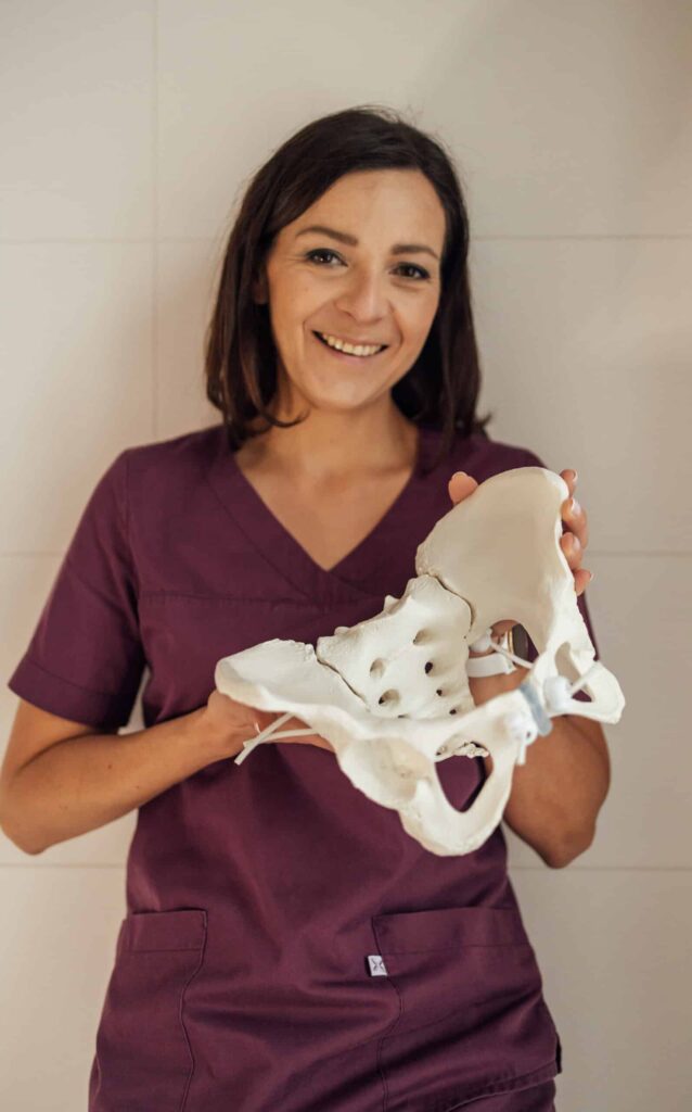 Marta Mszanowska, położna, stoi i trzyma model miednicy.