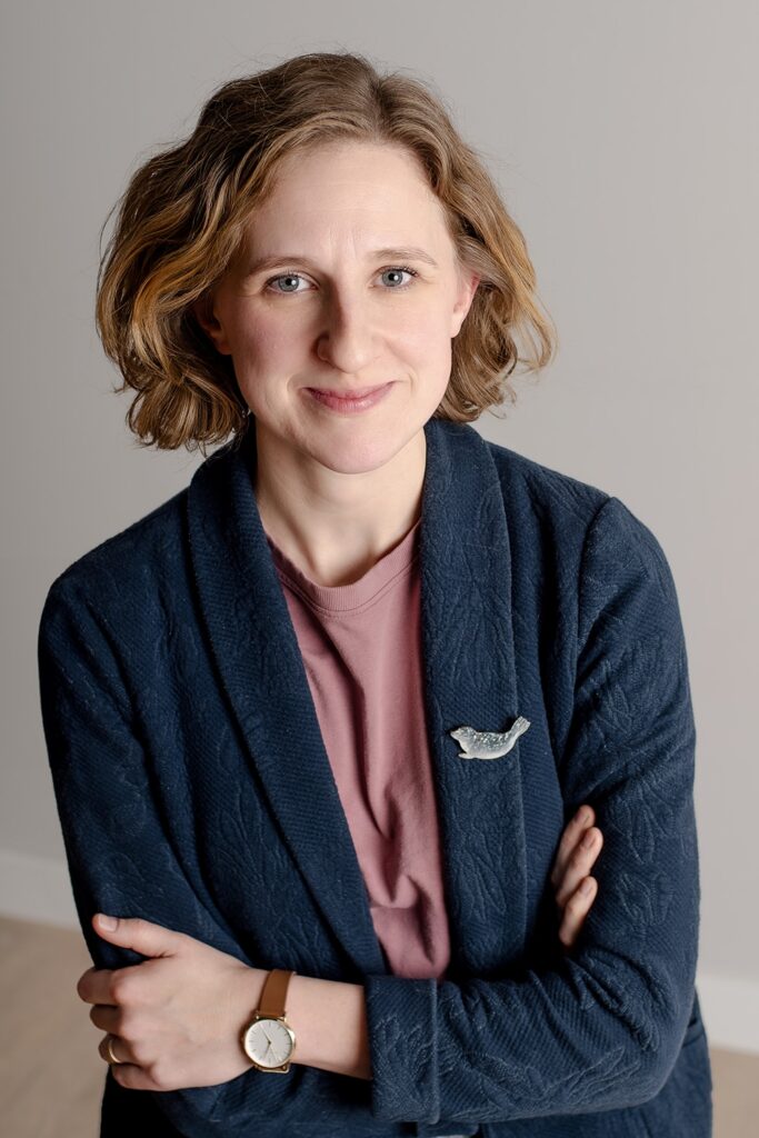 Anna Stolaś, psycholożka, stoi z założonymi rękami i uśmiecha się.